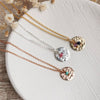 gold, silver and rose gold necklaces with birthstone charms laid on a ceramic dish with dried flowers