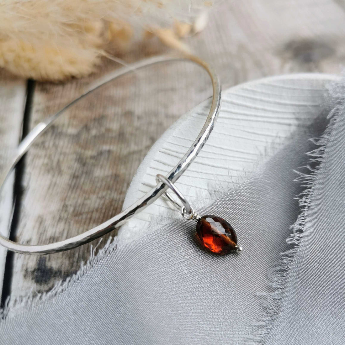 handmade silver bangle with a faceted garnet charm, by Cat Birch