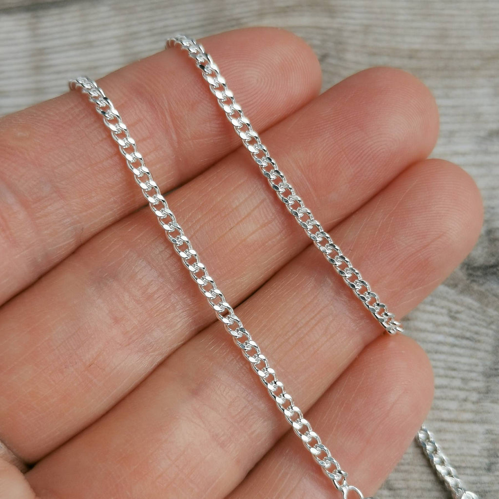 2mm silver curb chain for men draped over fingertips
