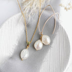 A set of gold and ivory baroque pearl earrings and a matching necklace laid out on a white surface, with the pearl earrings hanging from 14 carat gold-filled hooks and the necklace with a 14k gold-filled chain.