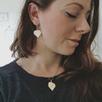 Woman wearing birch leaf-shaped earrings and a necklace with a neutral background