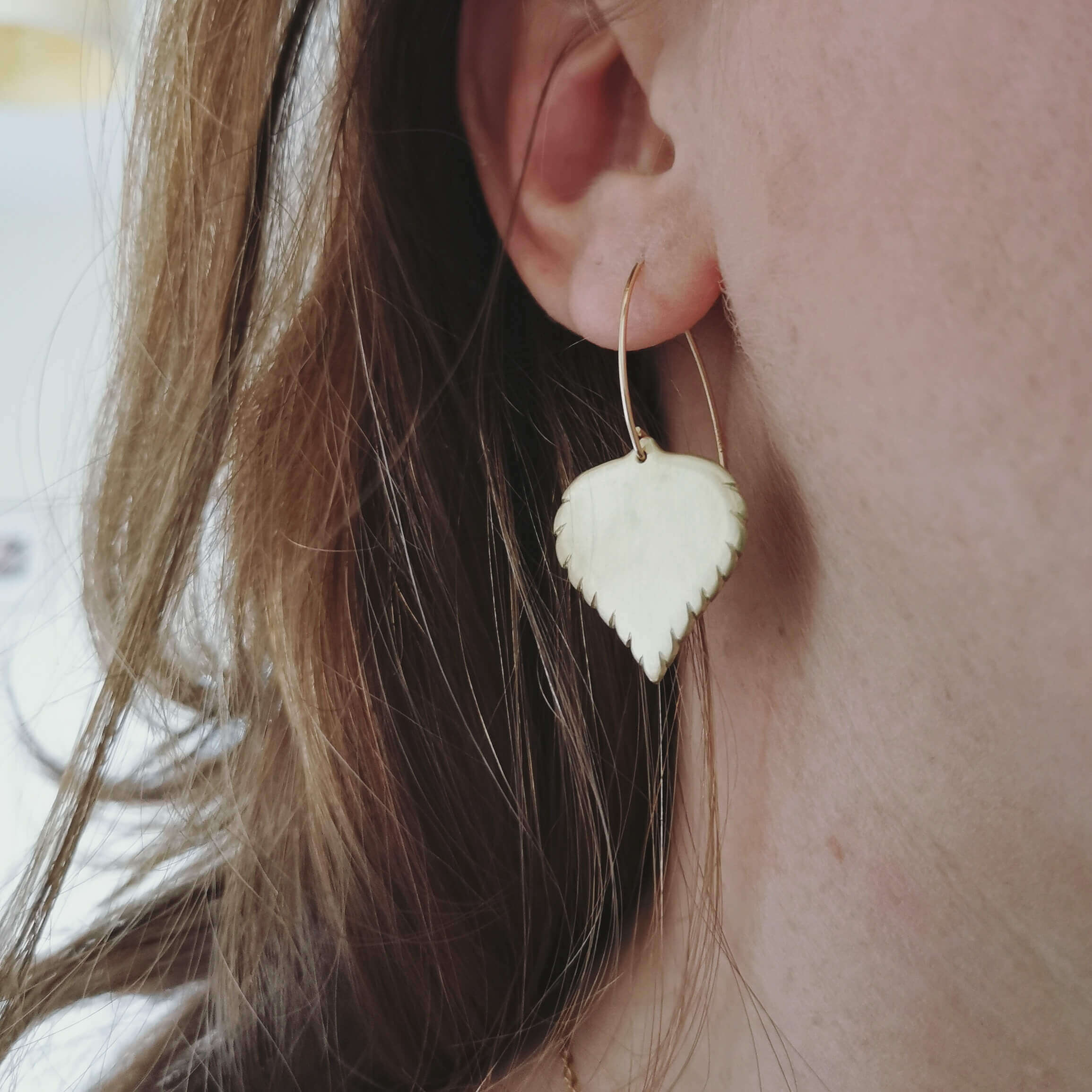 Close-up of a person wearing a delicately handmade birch leaf-shaped earring in solid brass
