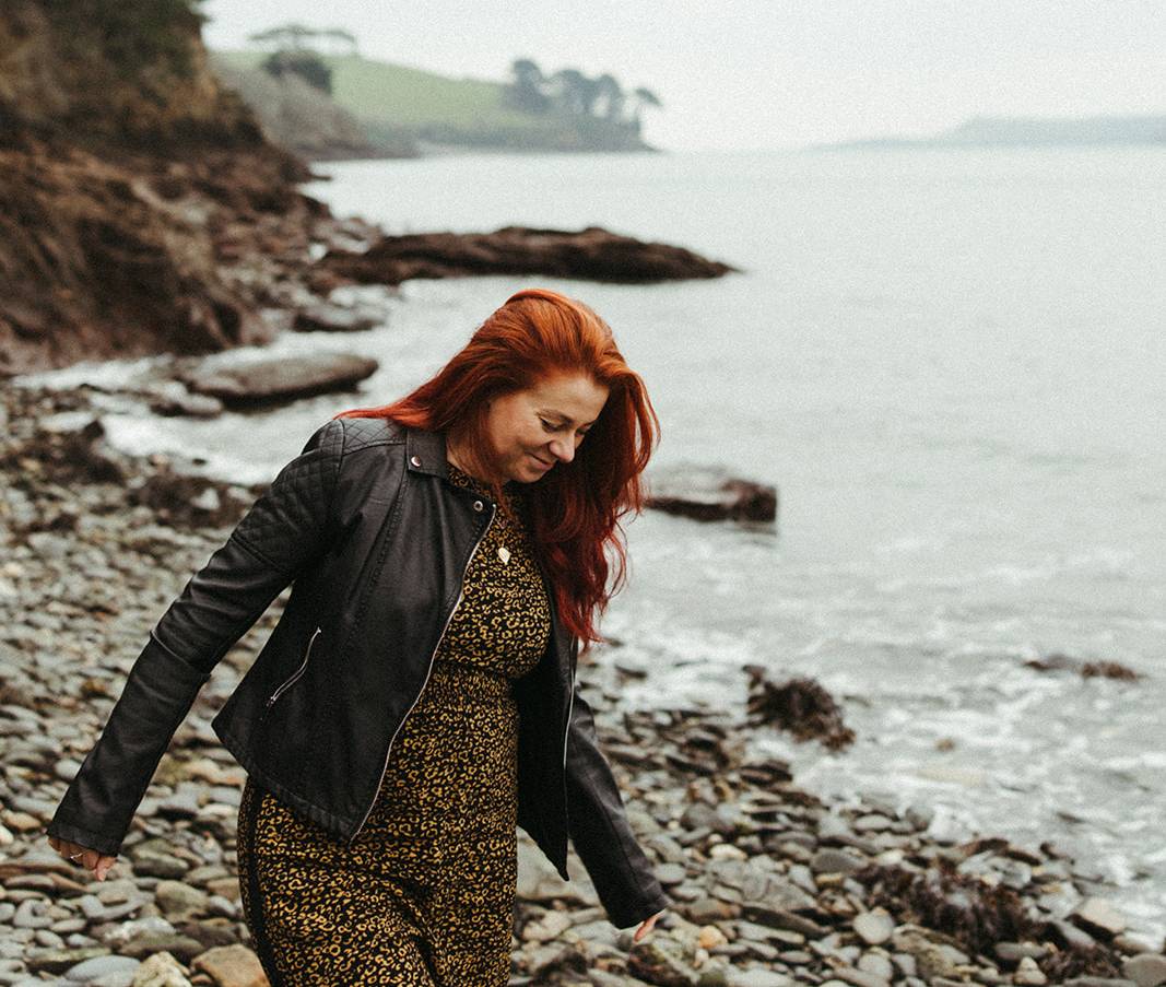 Woman with red hair standing on a rocky beach by the Helford River in Cornwall
