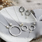 Silver jewelry set with necklaces and earrings on a textured surface