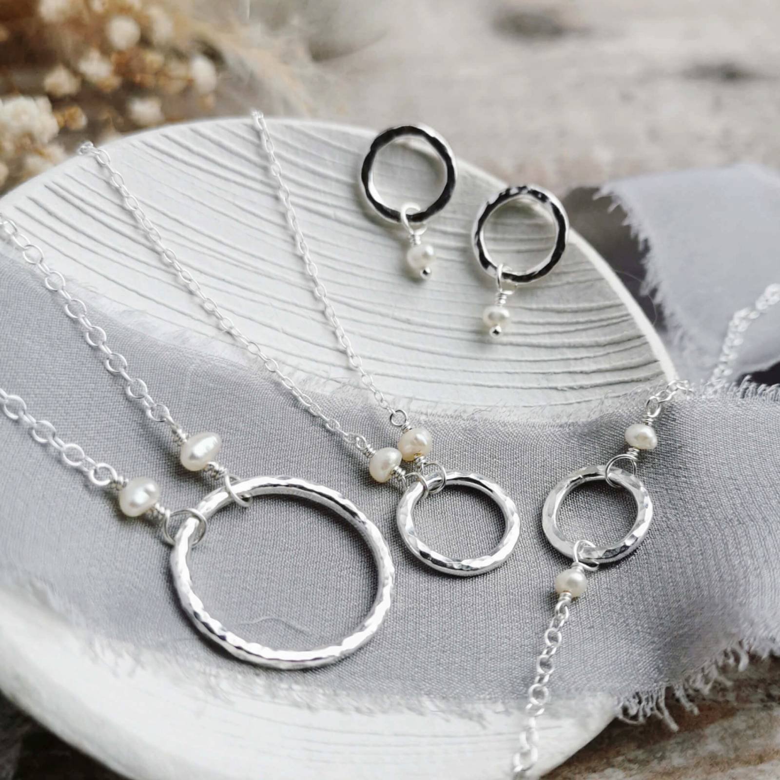 Silver jewelry set with necklaces and earrings on a textured surface