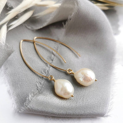 Gold pearl drop earrings on a grey silk 
background