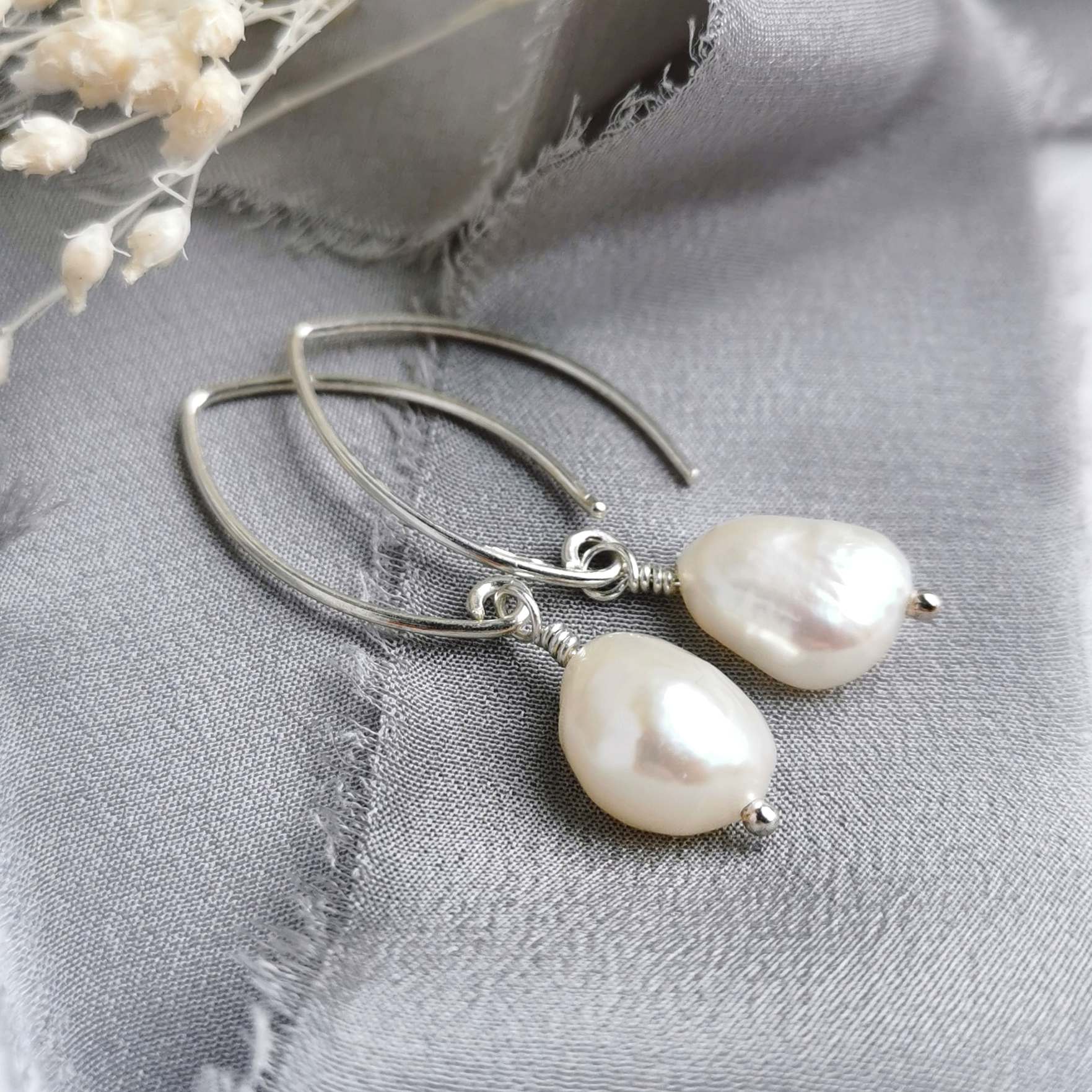 Pearl and silver earrings on a grey fabric background with white flowers.