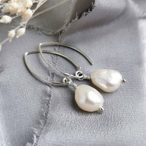 Pearl and silver earrings on a grey fabric background with white flowers.
