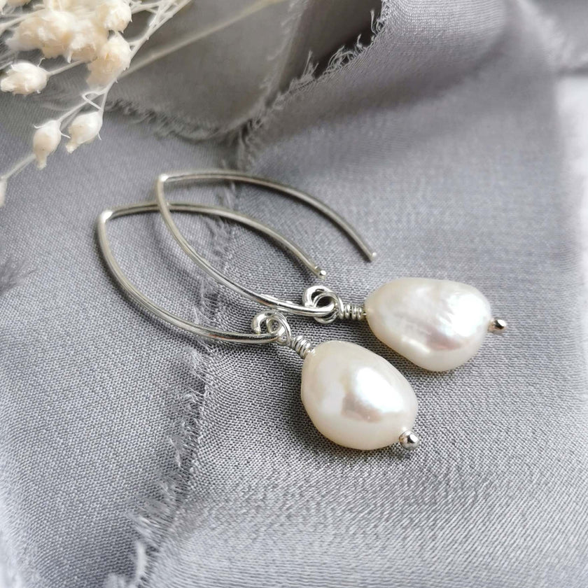 Pearl and silver earrings on a grey fabric background with white flowers.