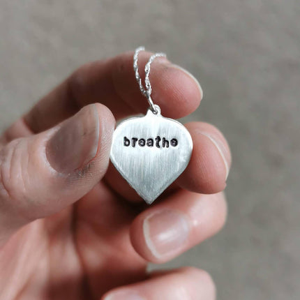 silver birch leaf necklace with breathe stamped onto the back, held in the fingers