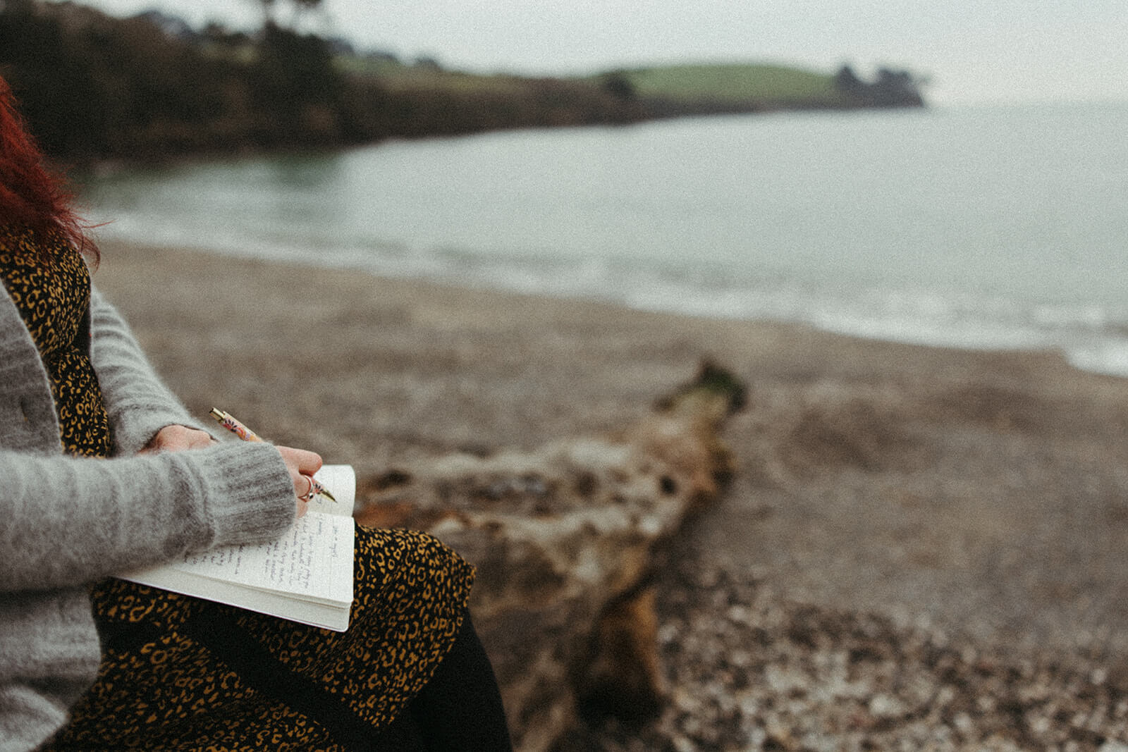 Cat Birch jeweller writing in her journal on a cornish beach with a blurred background