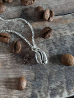 Silver necklace with a coffee bean charm on a wooden surface with coffee beans.