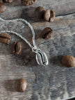 Silver necklace with a coffee bean charm on a wooden surface with coffee beans.