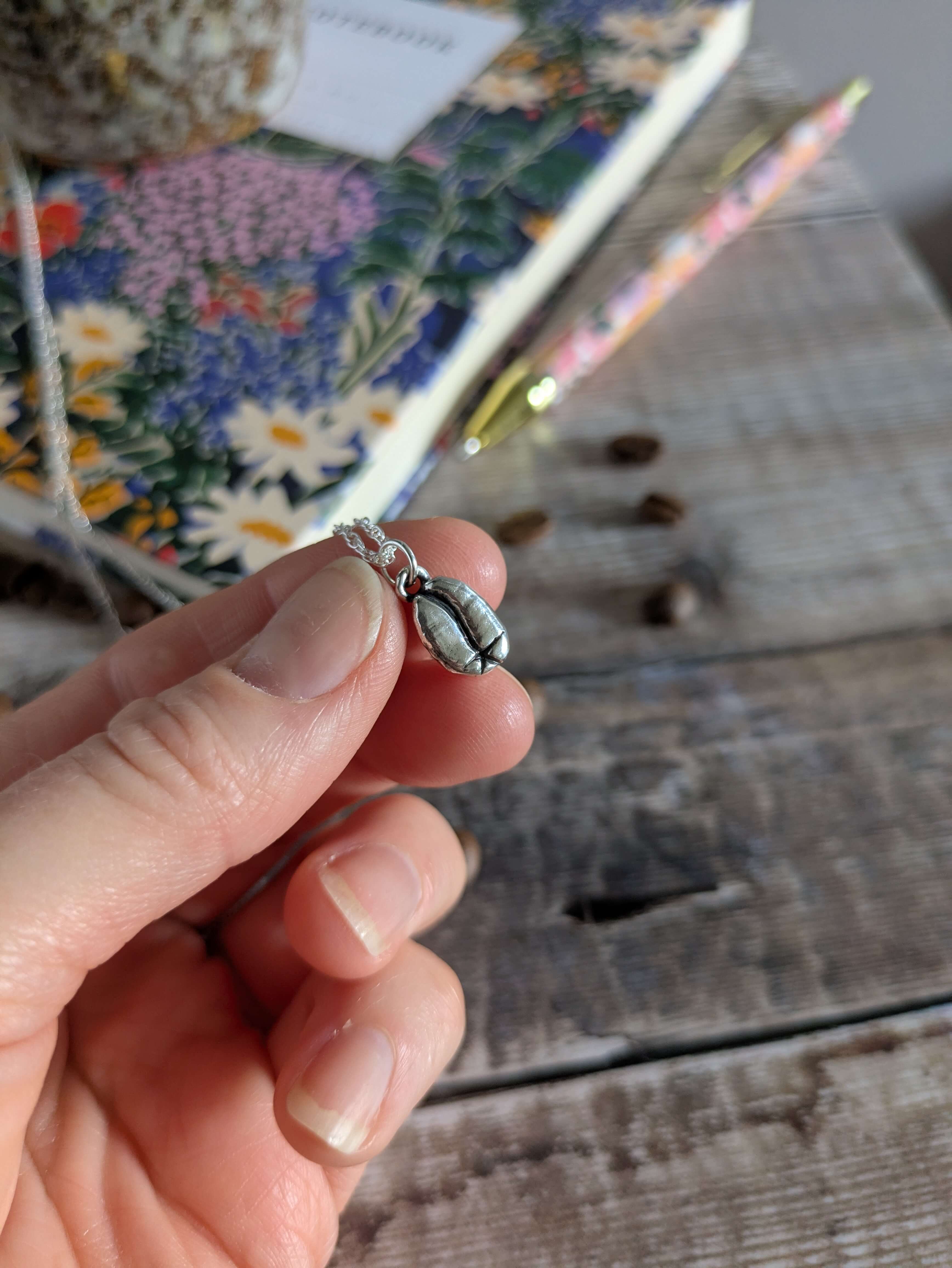 Hand holding a small silver necklace with a coffee bean charm