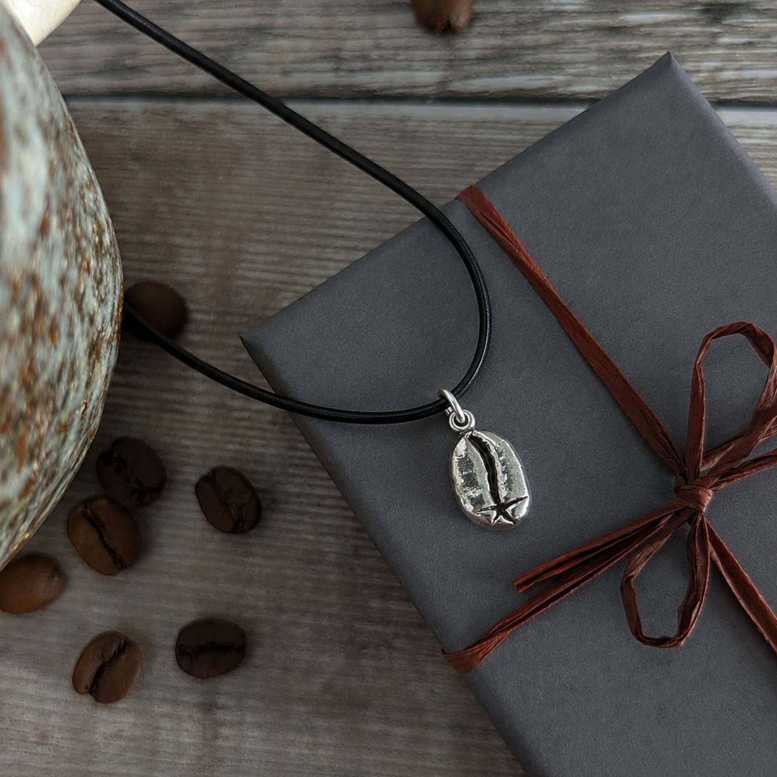 Necklace with a coffee bean pendant on a wrapped gift box with coffee beans around