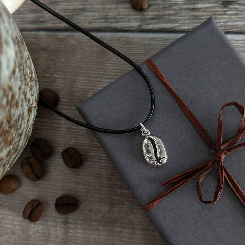 Necklace with a coffee bean pendant on a wrapped gift box with coffee beans around