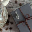 Silver necklace with a coffee bean pendant on a wrapped gift box with coffee beans around.
