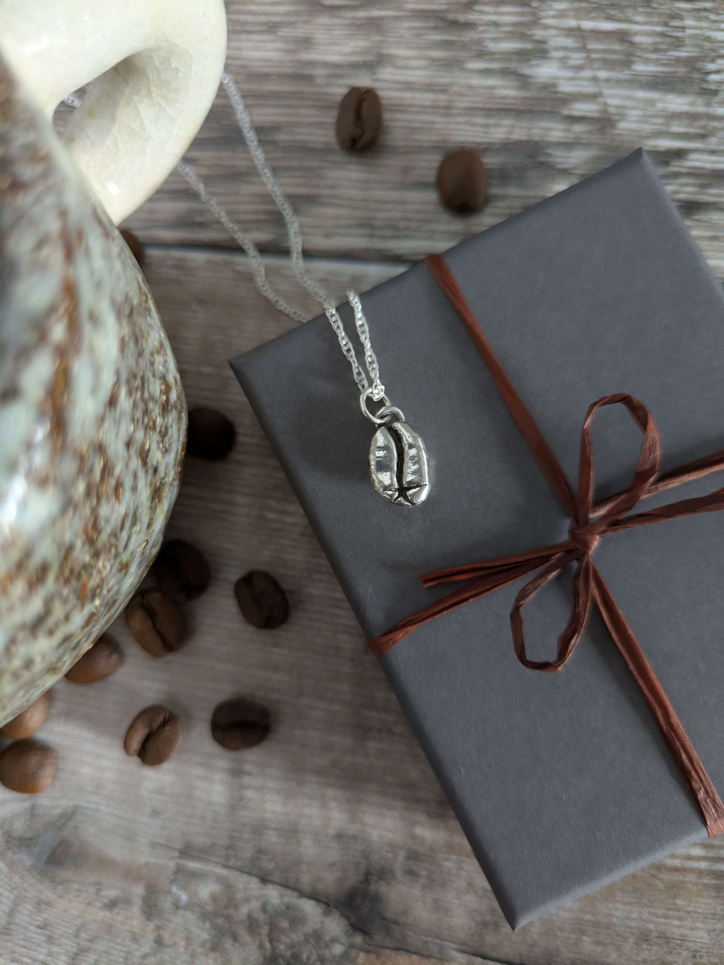 Necklace with a pendant on a wrapped gift box next to coffee beans and a mug on a wooden surface