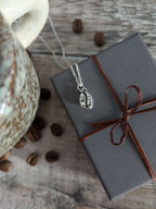 Necklace with a pendant on a wrapped gift box next to coffee beans and a mug on a wooden surface