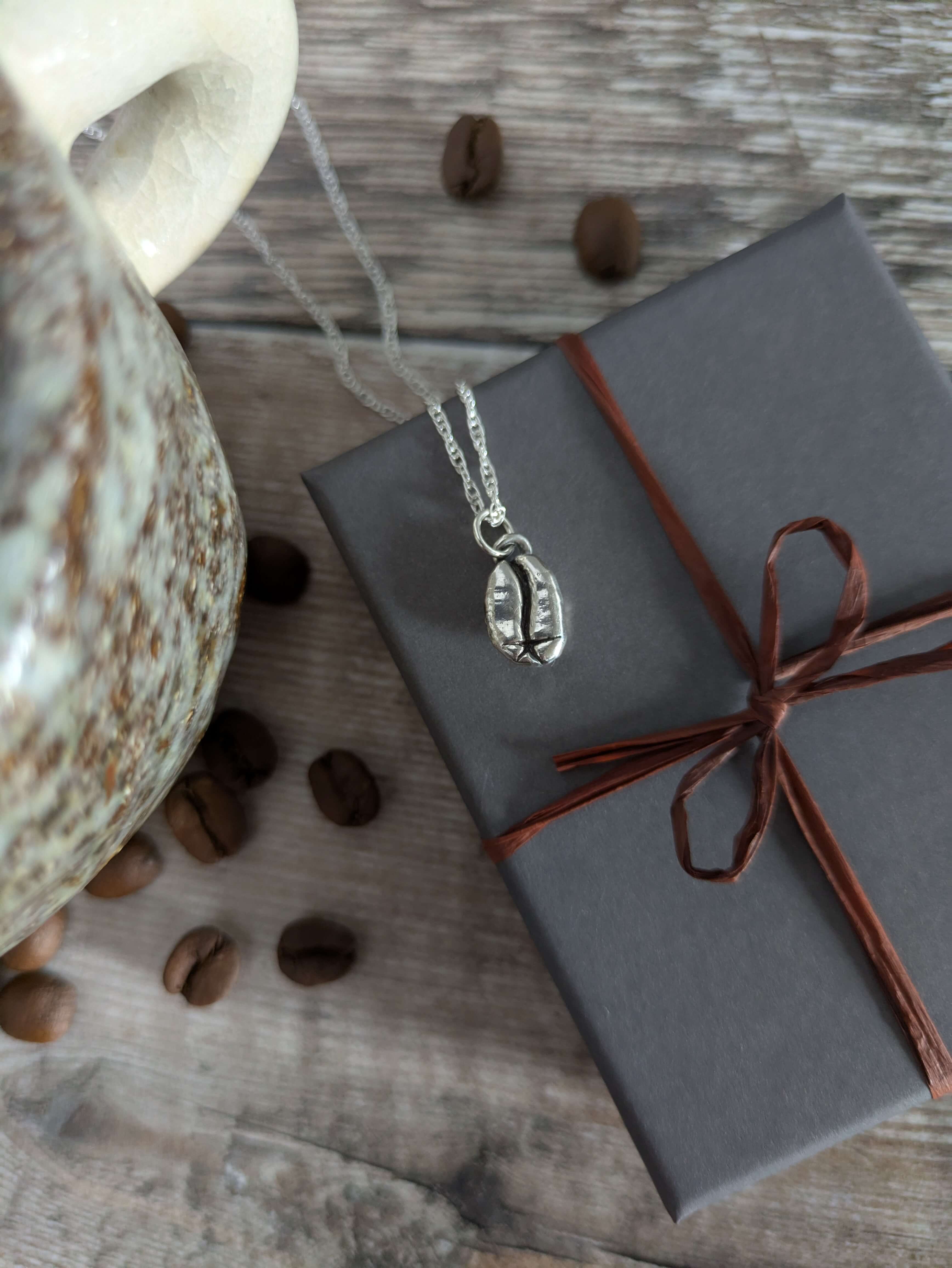 Necklace with a pendant on a wrapped gift box next to coffee beans and a mug on a wooden surface