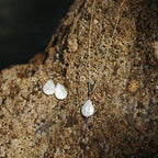 A set of 14k gold-filled necklace and matching drop earrings with ivory teardrop pearls, displayed on a textured brown rock covered in barnacles in cornwall, UK.