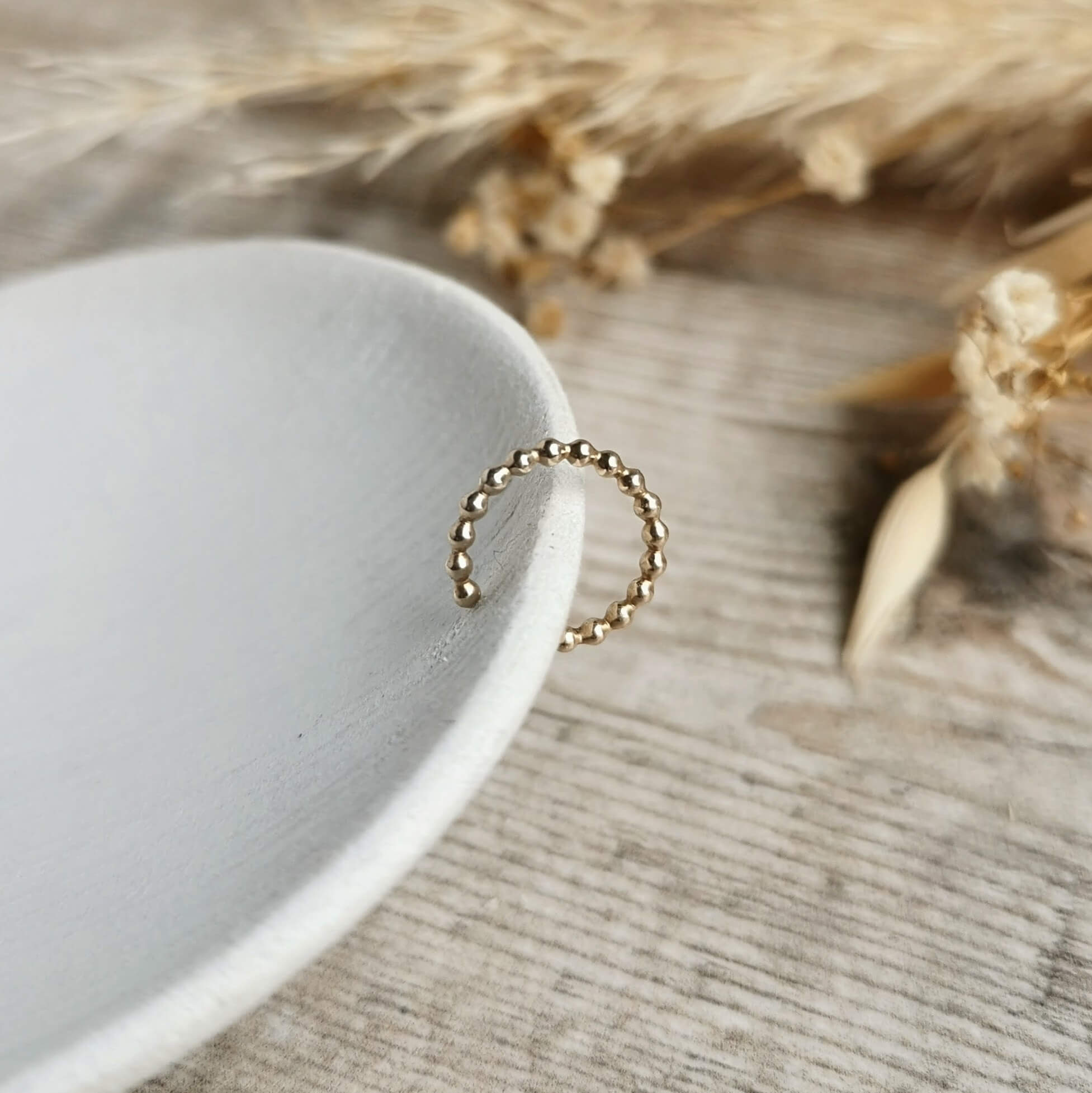 beaded Gold ear cuff on a white dish with dried plants in the background