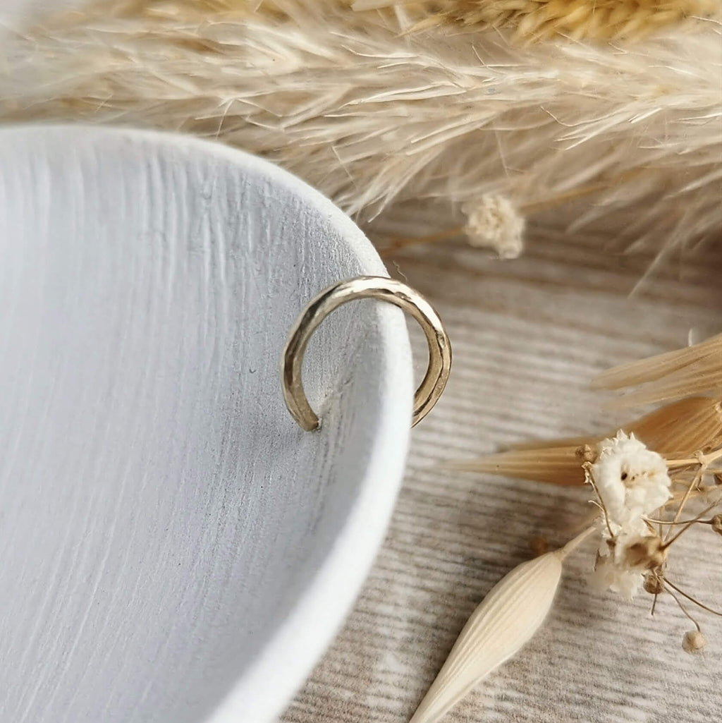 hammered Gold ear cuff on a white ceramic plate with dried flowers in the background