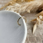 handmade Gold ear cuff on a white ceramic dish with dried plants in the background