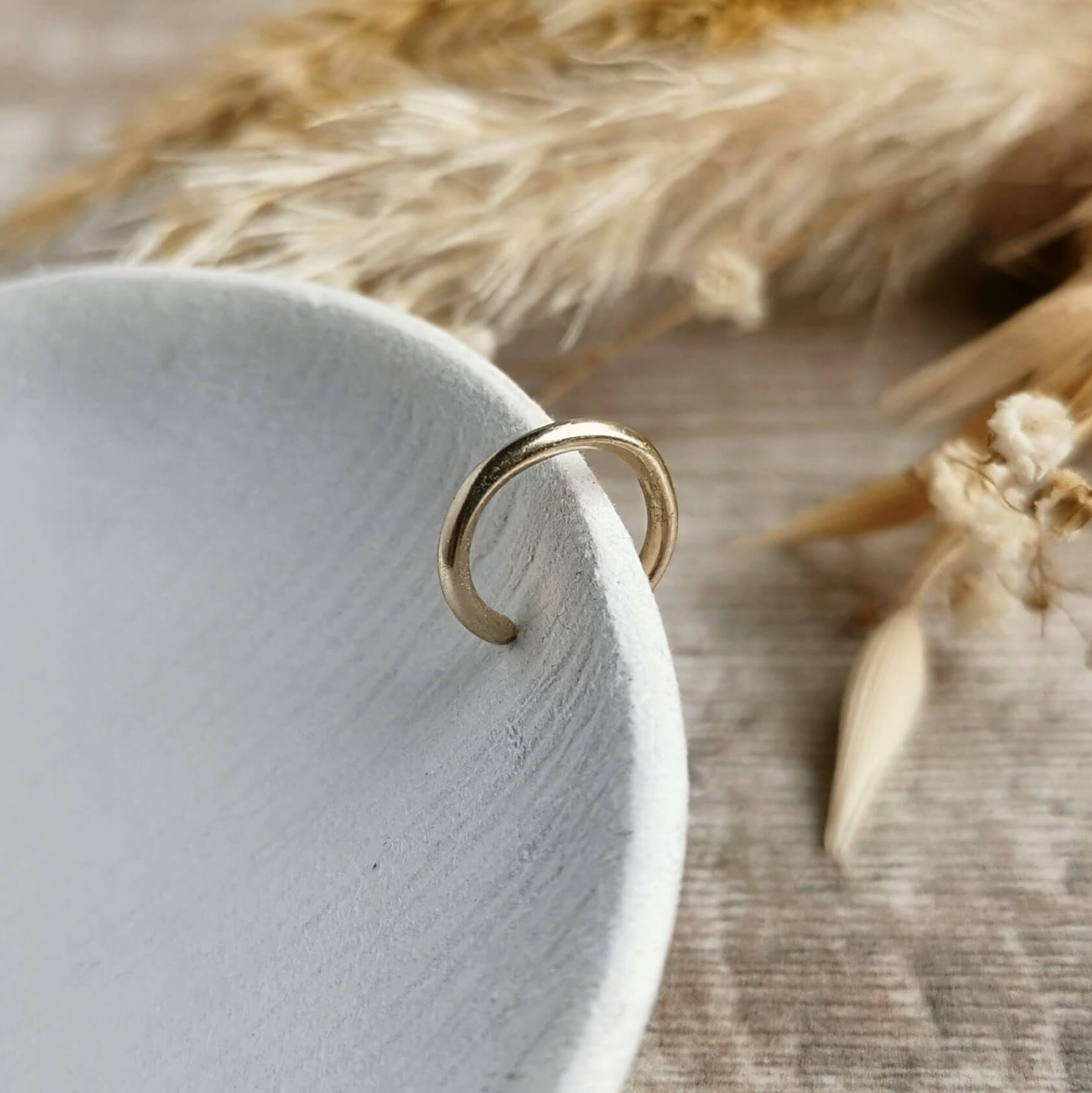 handmade Gold ear cuff on a white ceramic dish with dried plants in the background