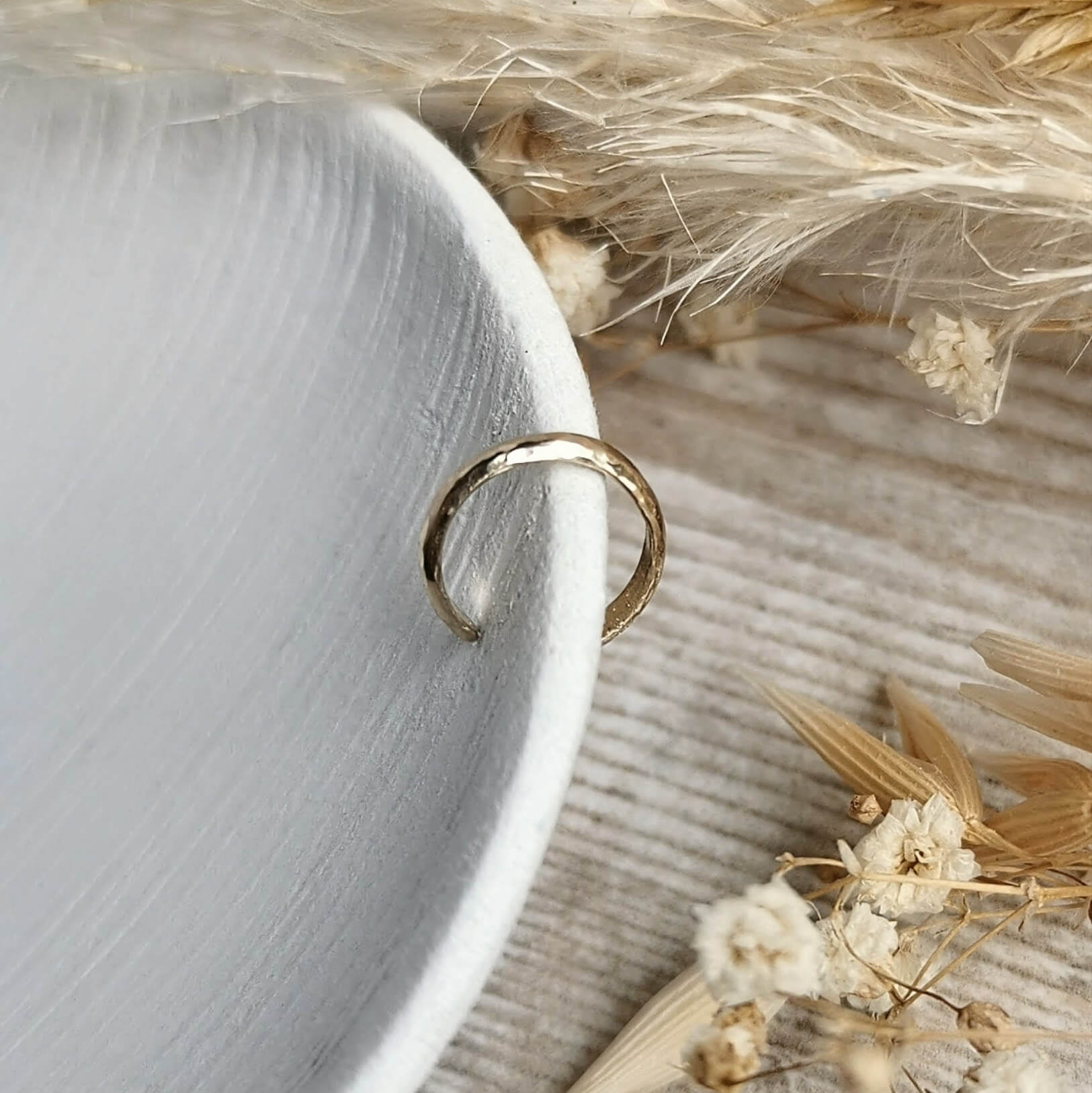 lightweight handmade hammered Gold ear cuff on a textured surface with dried flowers 