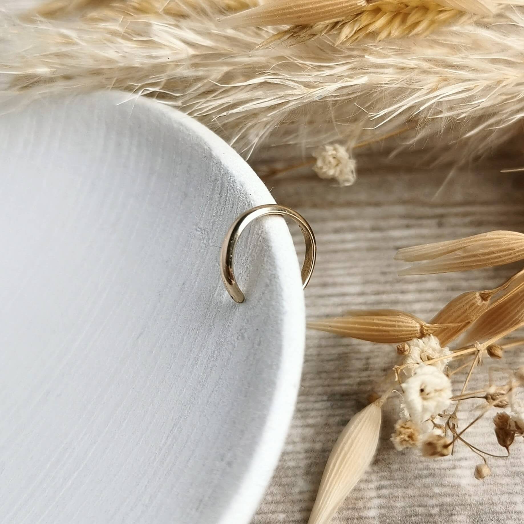 lightweight smooth Gold ear cuff on a white cloth with dried flowers in the background
