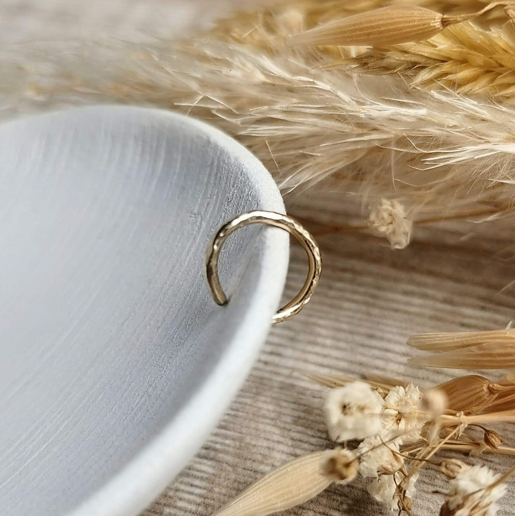 hammered Gold ear cuff on a white surface with dried flowers.