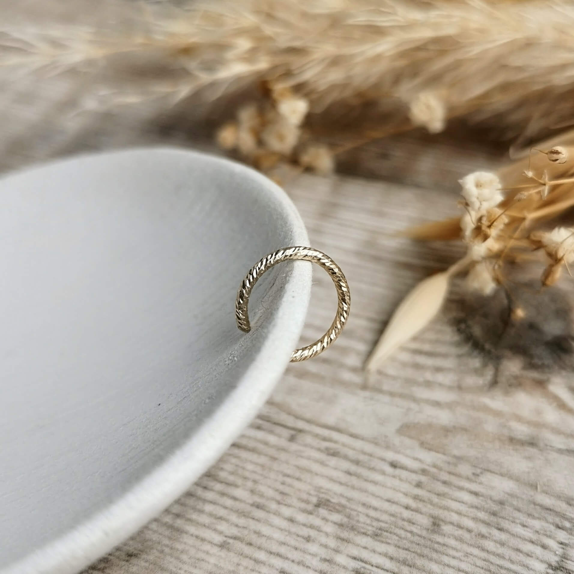rope texture Gold ear cuff on a white ceramic plate with dried plants in the background