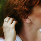 A close-up of a person's ear wearing two delicate gold ear cuffs, with red hair and a hand touching the hair in the background.