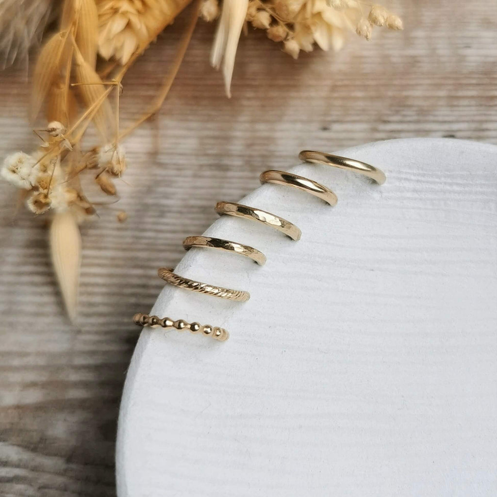 handmade Gold ear cuffs stacked on a white dish with dried flowers in the background