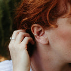 woman with wavy red hair wearing a gold beaded decorative ear cuff and a hammered silver ear cuff and tucking her hair behind her ears