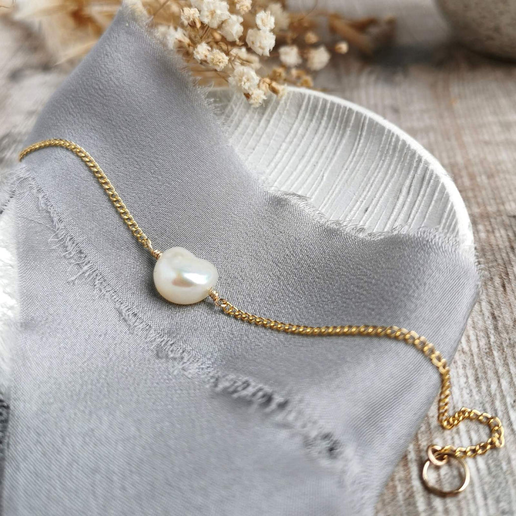 Gold bracelet with an ivory baroque pearl on a gray fabric background
