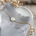 Gold bracelet with an ivory baroque pearl on a gray fabric background