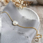 Gold bracelet with an ivory baroque pearl on a gray fabric background