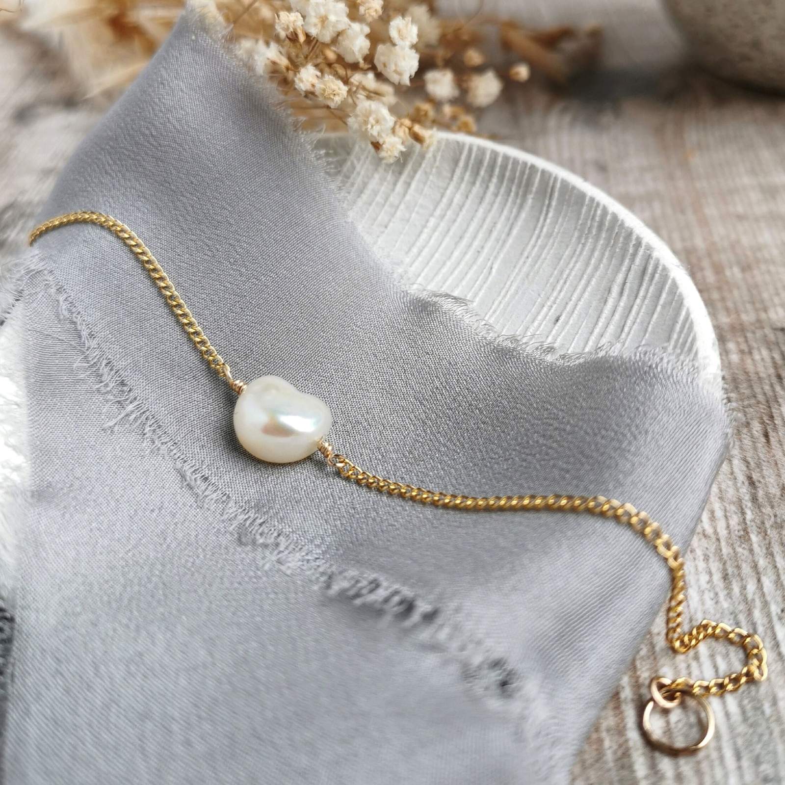 Gold bracelet with an ivory baroque pearl on a gray fabric background