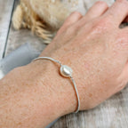A close-up of a person's wrist wearing a delicate handmade silver chain bracelet with a single ivory white freshwater baroque pearl.