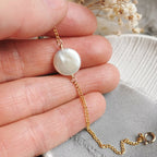 ivory coin Pearl bracelet with gold chain held between fingers on a neutral background
