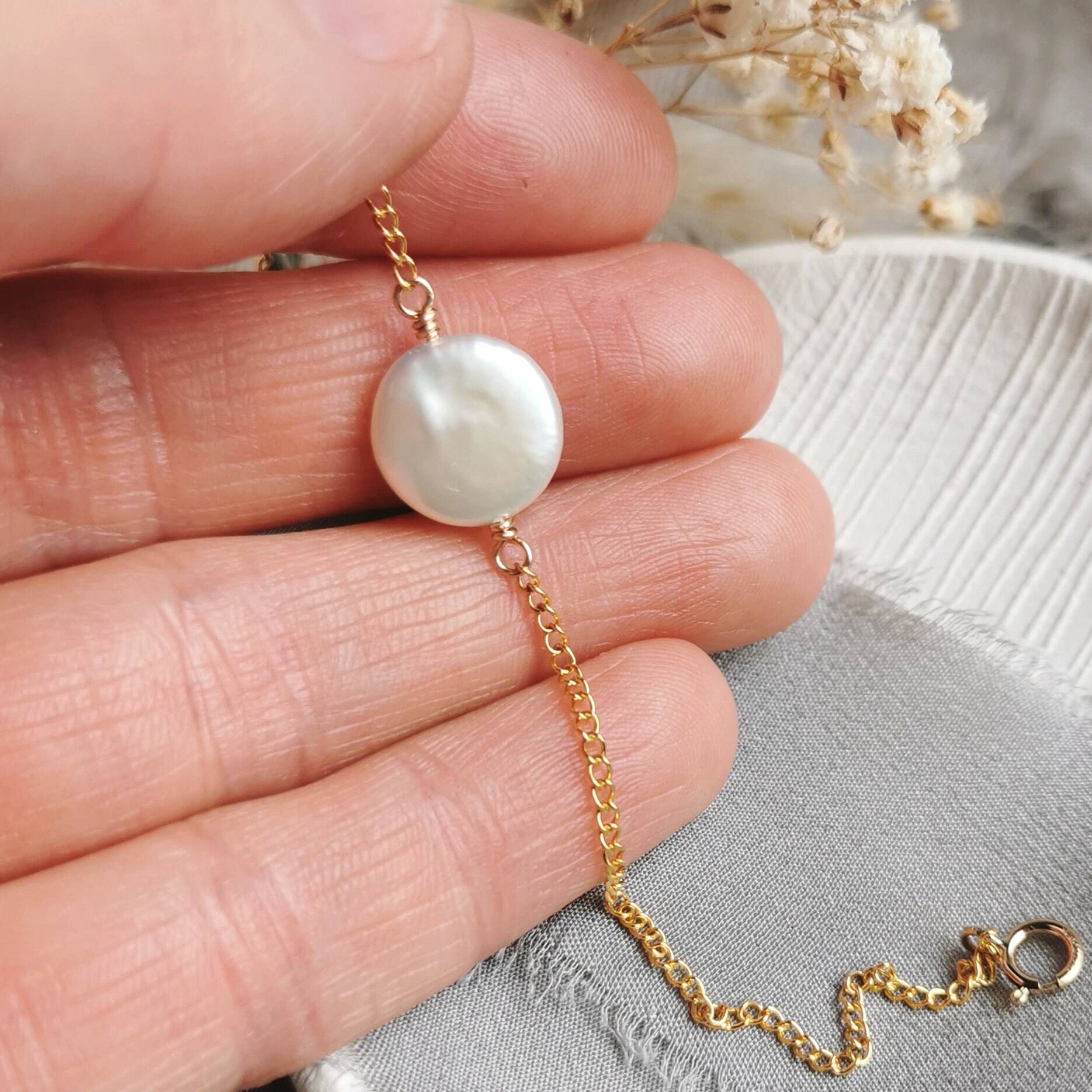 ivory coin Pearl bracelet with gold chain held between fingers on a neutral background