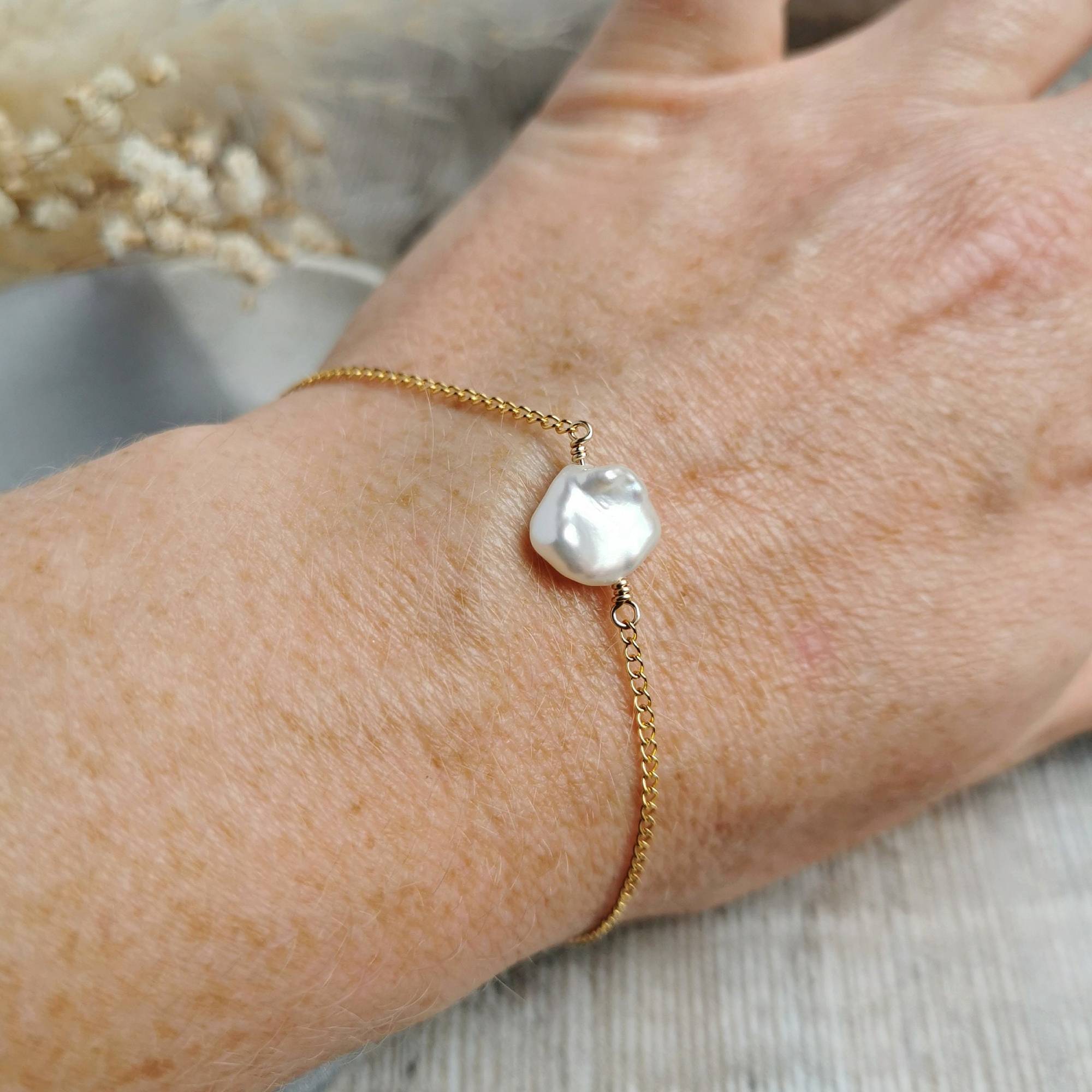 Gold bracelet with a unique pearl worn on a wrist against a neutral background