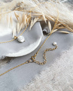 pearl and gold pendant with 2 inch extender chain with pearl detail, laid on a textured surface with dried leaves.