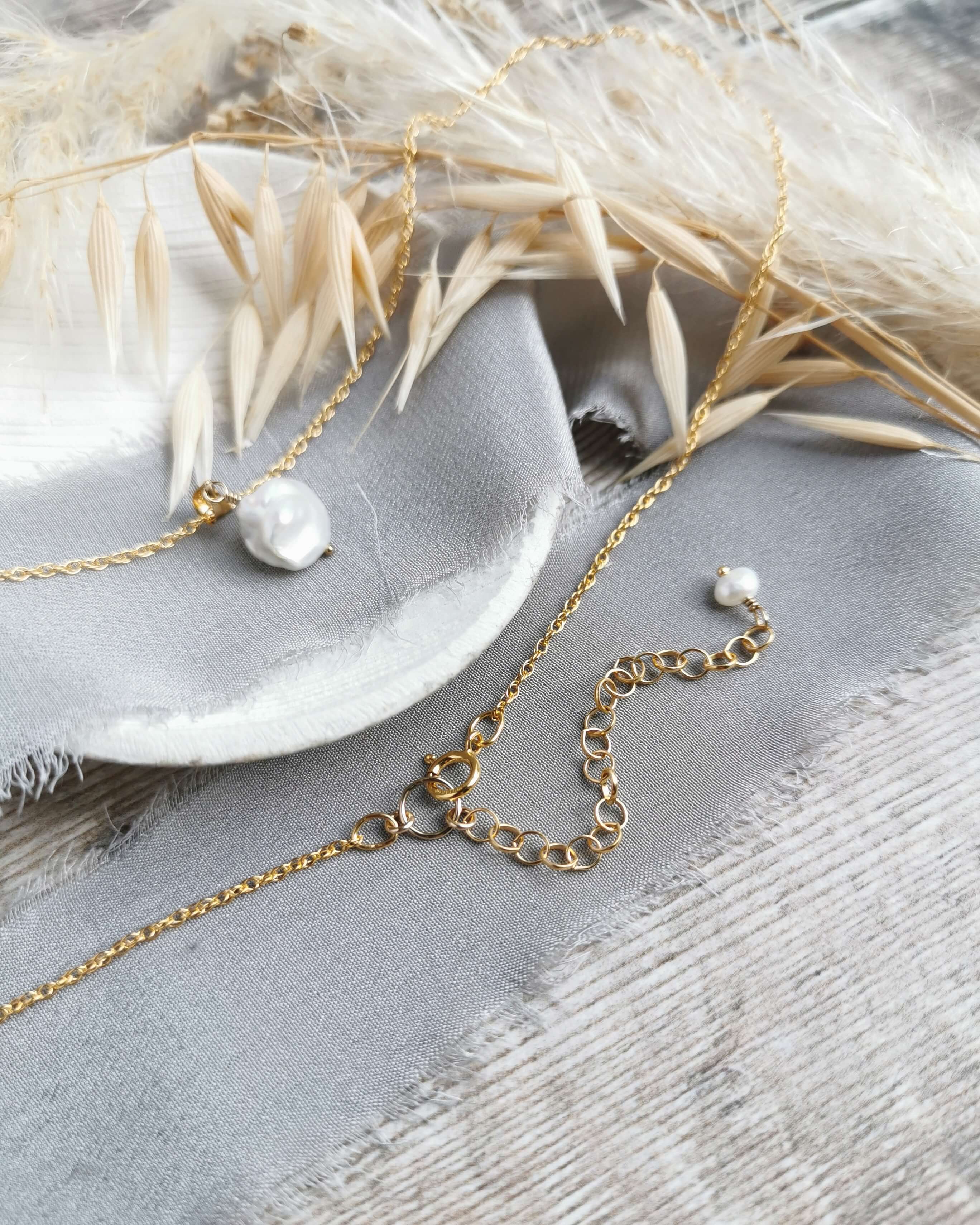 pearl and gold pendant with 2 inch extender chain with pearl detail, laid on a textured surface with dried leaves.