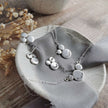 Silver necklace with clusters of silver shapes with words of affirmations stamped into them, lying on a dish with grey ribbon with dried flowers in the background