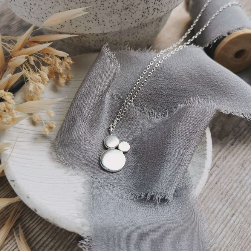 Silver necklace with circular shapes in a cluster on a textured fabric surface