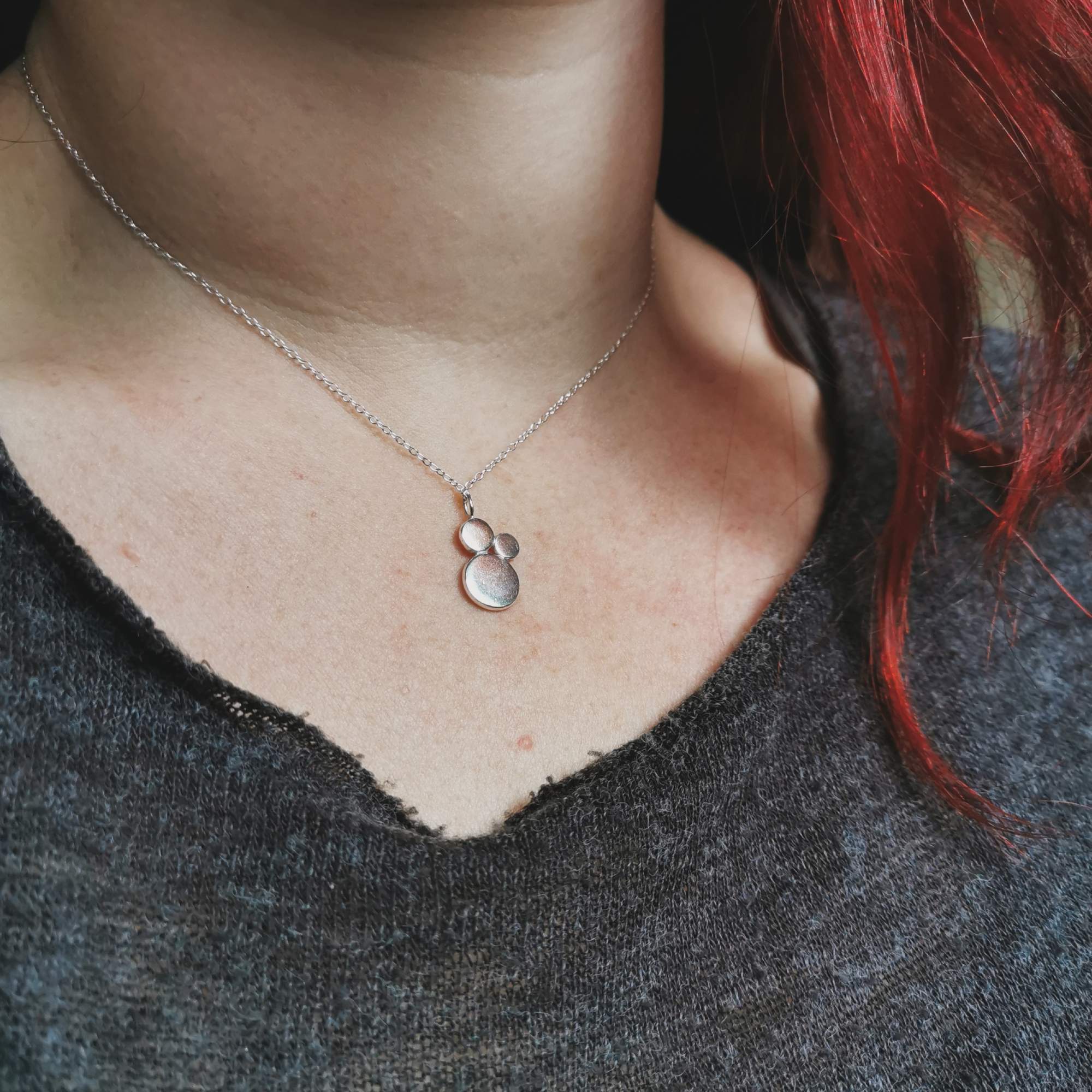 Necklace with a silver pendant worn by a woman with red hair, close-up shot.