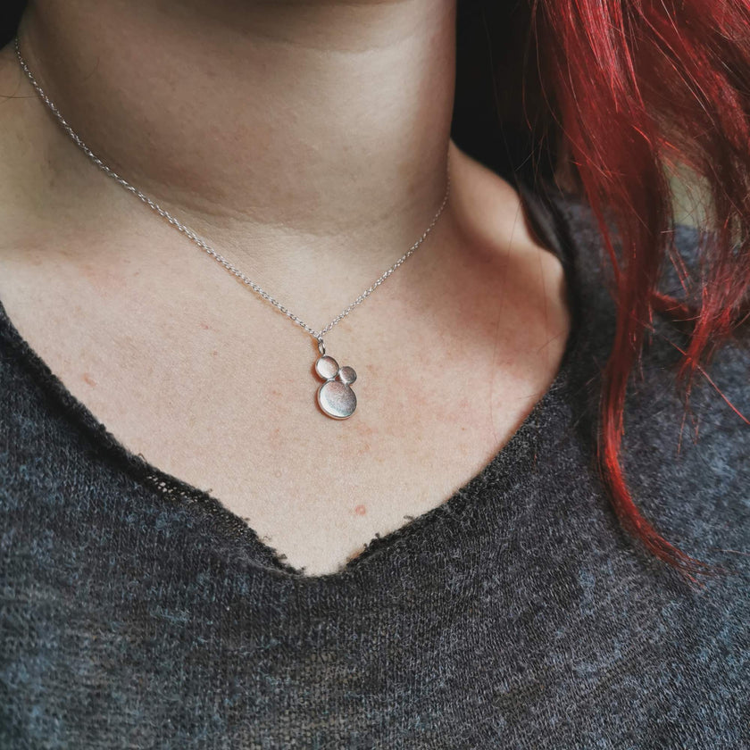 Necklace with a silver pendant worn by a woman with red hair, close-up shot.
